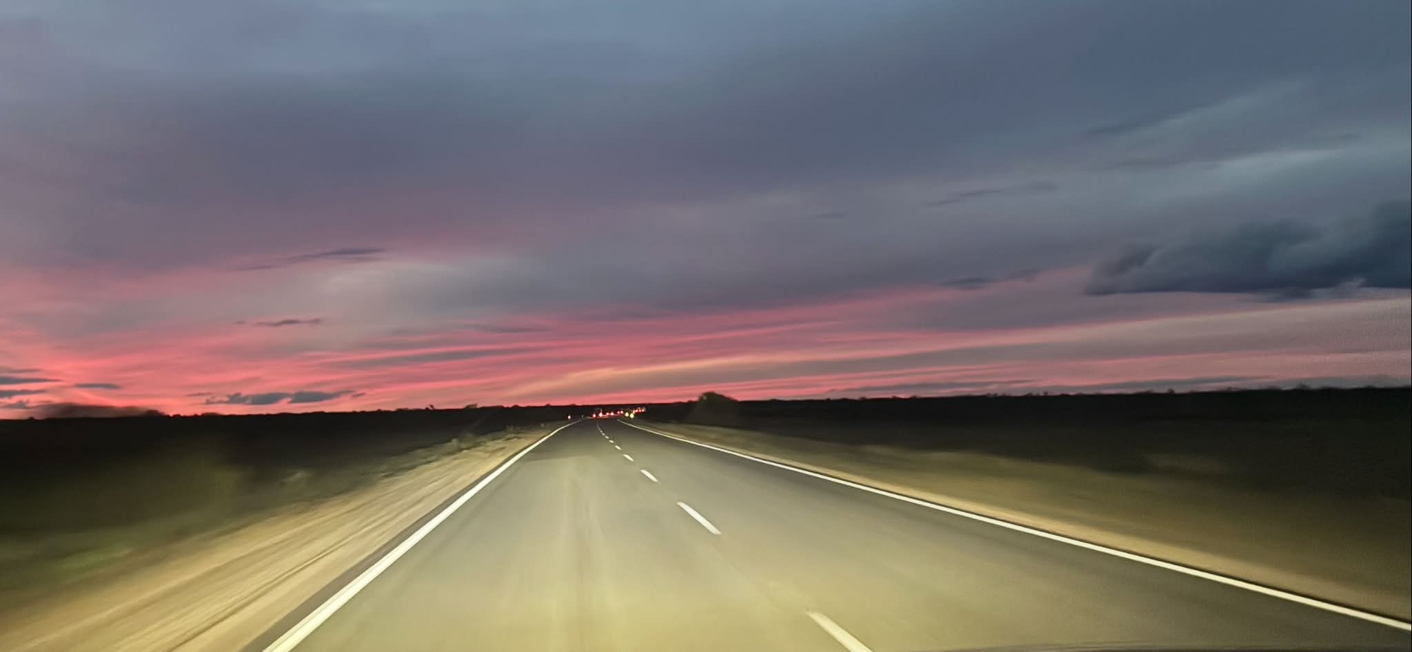Uluru expedition convoy driving at dusk under a pink sunset sky